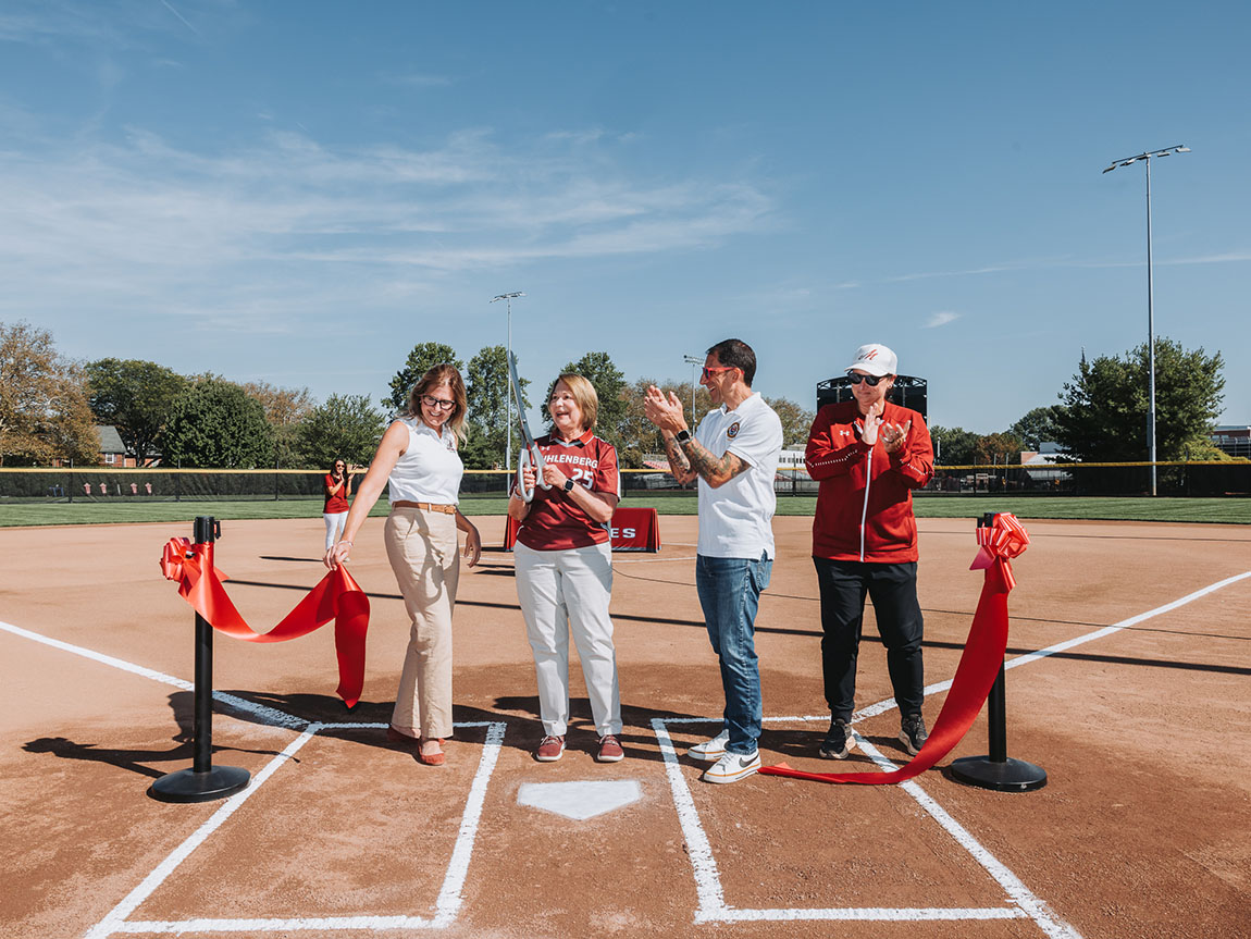 Four people cut the ribbon on a new softball field on a sunny day